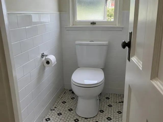 Clean white toilet in a tiled bathroom with hex floor and frosted window in Rose Bay