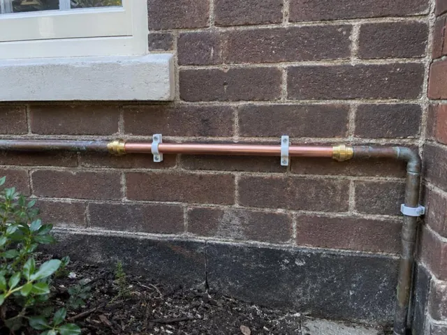 Repaired copper water pipe on a brick exterior wall beneath a window in Edgecliff